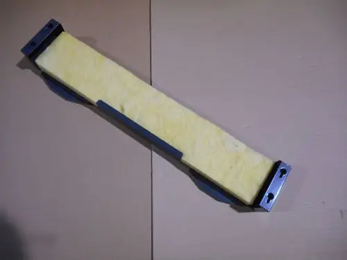 Remeha unteres Verkleidungstück mit gelbem Dämmmaterial und Metallbefestigungen, flach und länglich, auf einem neutralen Hintergrund liegend.